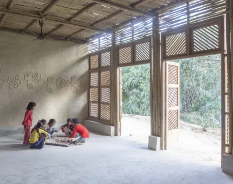 Einige Kinder spielen auf dem Boden eines hellen, nachhaltig gebauten Raumes mit großen Holztüren und dekorativen Wänden.