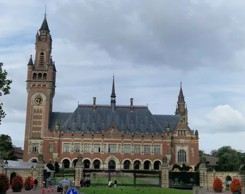 Der Friedenspalast in Den Haag, ein beeindruckendes historisches Gebäude mit einem großen Turm und einer gepflegten Gartenanlage, unter einem bewölkten Himmel.