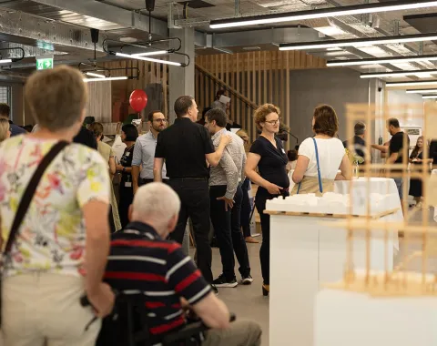 Besucherinnen und Besucher erkunden den neuen Standort der Universität Liechtenstein während des Tags der offenen Tür. Menschen stehen in einem modernen Innenraum, unterhalten sich und betrachten Ausstellungsstücke.