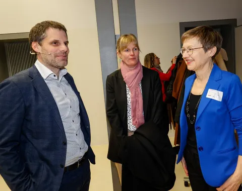 Drei Personen unterhalten sich bei einer Veranstaltung an der Universität Liechtenstein. Eine Frau trägt einen blauen Blazer, eine andere einen schwarzen Mantel mit rosa Schal, und der Mann trägt ein dunkelblaues Sakko.