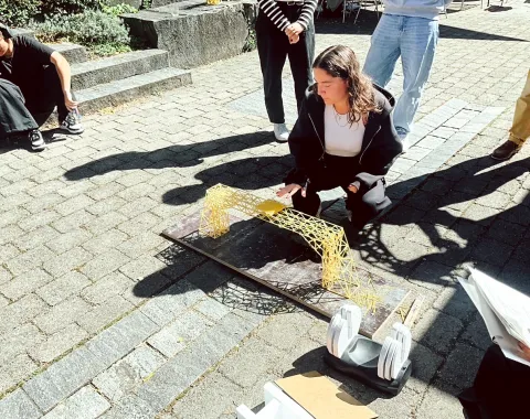 Studierende testet Tragfähigkeit von Spaghettibrücke