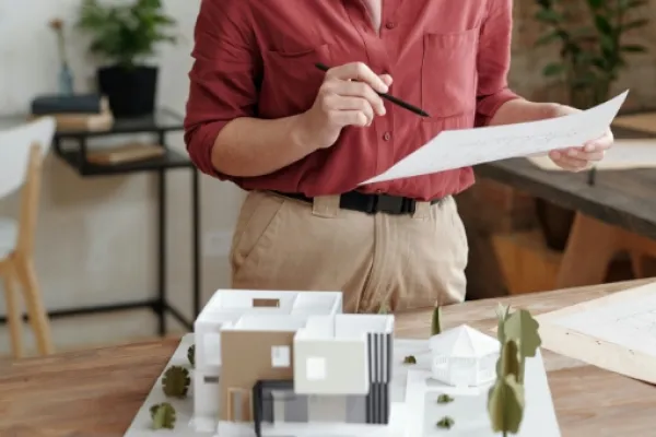 Eine junge Frau steht vor einem Tisch. Darauf steht ein Model eines kleinen Hauses.
