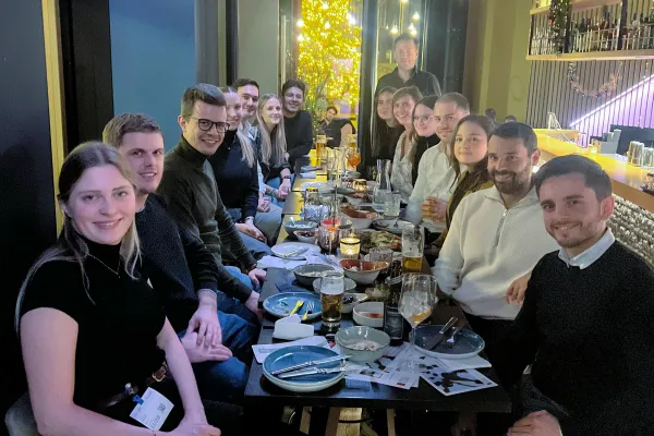 Große Gruppe junger Alumni sitzt beim Abendessen in einem Restaurant und tauscht sich über das Studium aus.