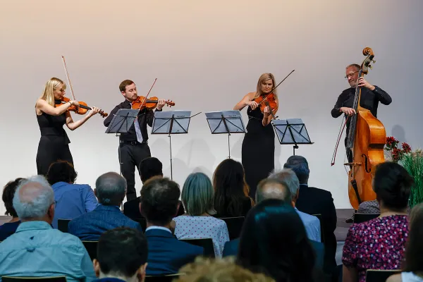 Streichquartett mit Kontrabass spielt vor Publikum auf einer Buehne im Rahmen einer feierlichen Veranstaltung.