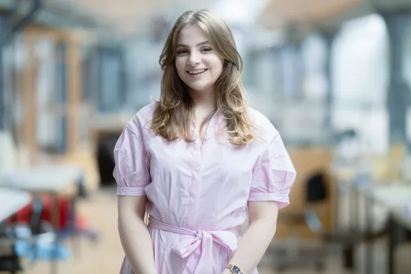 Studentin der Universität Liechtenstein im rosa Kleid lächelt in die Kamera – Campusaufnahme in freundlicher Lernumgebung