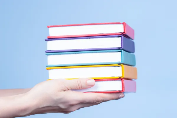 Hand haelt mehrere bunte Buecher vor hellblauem Hintergrund, Fokus auf Vielfalt und Bildung.