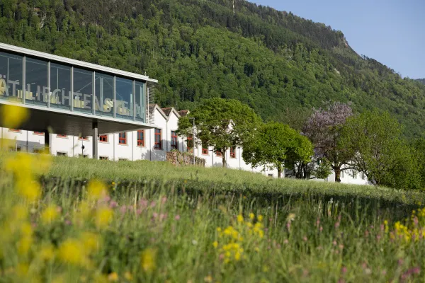 Gebäudereihe der Universität Liechtenstein im Grünen mit auffälligen roten Fensterrahmen und Blumenwiese.