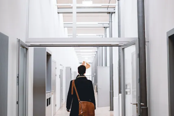 Studierende*r durchquert lichtdurchfluteten Hochschulflur der Universität Liechtenstein mit Dialektschrift an der Decke – modernes Campusambiente mit regionalem Bezug.