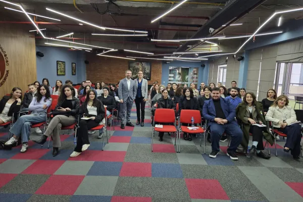 Seminarraum mit Studierenden und Dozenten, die an einem Cybercrime-Seminar teilnehmen. Die Teilnehmenden sitzen auf roten Stühlen in einem modernen Raum mit geometrischem Teppichmuster und futuristischer Beleuchtung.