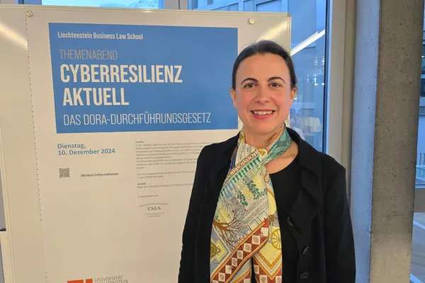 Frau steht lächelnd vor einem Plakat der Liechtenstein Business Law School. Das Plakat kündigt den Themenabend „Cyberresilienz aktuell: Das DORA-Durchführungsgesetz“ an, der am 10. Dezember 2024 stattfindet.