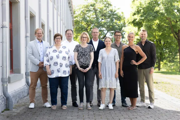 Team der Undergraduate and Graduate School der Universität Liechtenstein vor dem Campusgebäude in sonniger Umgebung