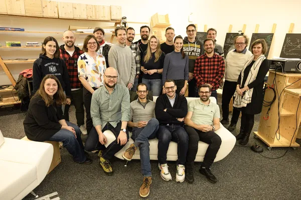 Gruppenfoto von Absolventen des Masterprogramms in Entrepreneurship der Universität Liechtenstein, die sich in einem Raum mit Regalen und Tafeln versammelt haben. Die Personen lächeln und stehen oder sitzen in zwei Reihen.