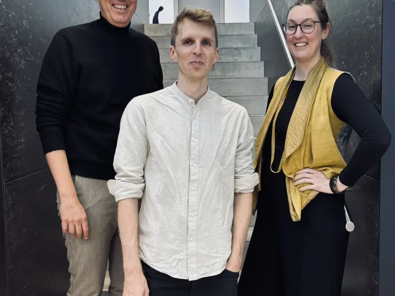 Drei Personen auf einer grau/schwarzen Treppe